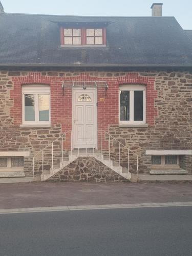a brick house with a white door and two benches at La Mancelliere in Isigny-le-Buat