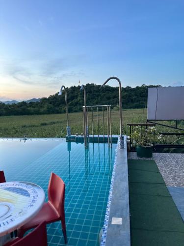 a swimming pool with a table and red chairs at Daiya Nirvana Pool Villa, Khao Yai in Klang Dong