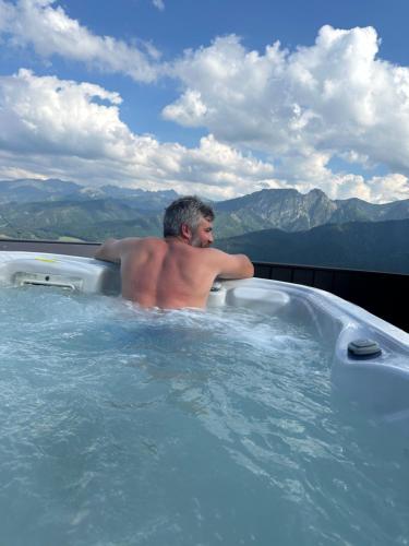 a man sitting in a jacuzzi tub with mountains in the background at Dom Tatrzański Ewa Deluxe in Kościelisko