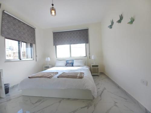 a white bedroom with a large bed and two windows at Shmeisani homes central location near Abdali in Amman