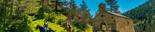 two men riding horses next to a stone building at Apartaments Sort Pirineus in Sort
