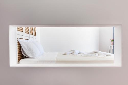 espejo que refleje una cama con sábanas y almohadas blancas en Aegeo Hotel, en Chora Folegandros