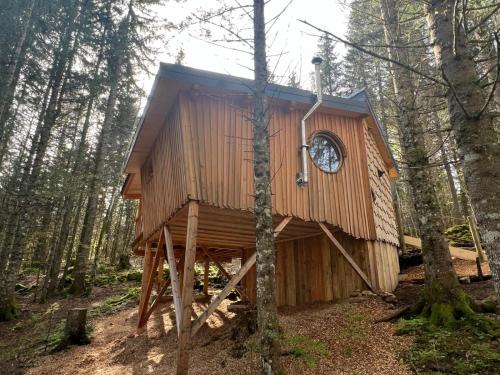 a tree house in the woods with a clock on it at Les Écrins du Val de Mouthe, JURA in Petite Chaux