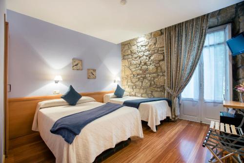 a hotel room with two beds and a stone wall at Pensión Nuevas Artes in San Sebastián