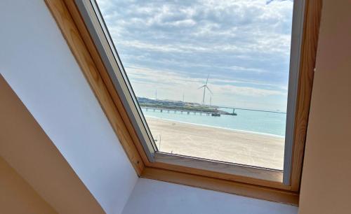 une fenêtre avec vue sur une plage avec un moulin à vent dans l'établissement La Sirena - Appartements Face Mer et Nausicaa, à Boulogne-sur-Mer