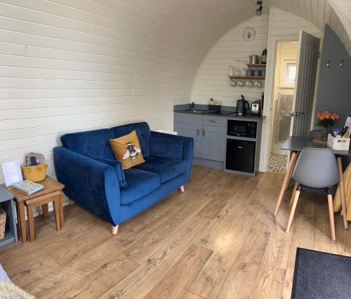 a living room with a blue couch and a kitchen at Cwt y Gwenyn Glamping Pod in Conwy