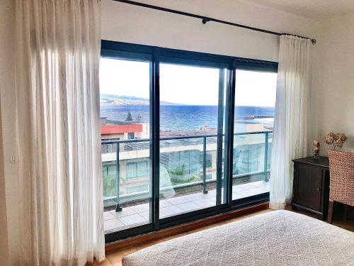 een slaapkamer met een groot raam met uitzicht op de oceaan bij Oceanus in Horta
