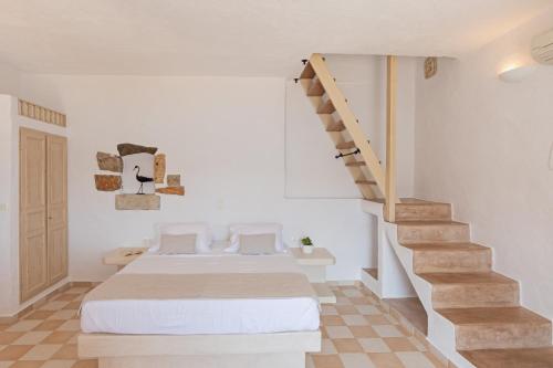 a white bedroom with a bed and a staircase at Kalderimi Residencies in Astypalaia Town