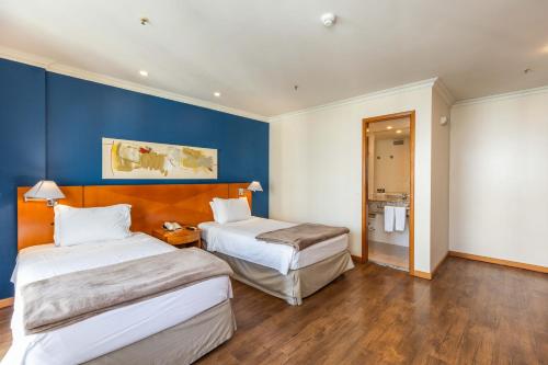 a hotel room with two beds and a blue wall at Barra Premium - flat com serviços, recepção 24 horas, piscina, academia e balsa para praia! in Rio de Janeiro