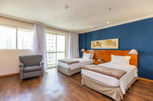 a hotel room with two beds and a chair at Barra Premium - flat com serviços, recepção 24 horas, piscina, academia e balsa para praia! in Rio de Janeiro