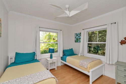 two beds in a room with two windows at Gorgeous Renovated 1937 Plantation Style Beach House 50 Steps to the Center of the Beach home in Kailua