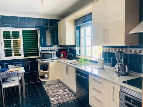 a kitchen with white cabinets and blue tiled walls at Vivenda Soares in Estômbar