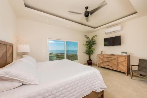 a bedroom with a white bed and a television at Casa De La Perla, Ocean View 4 Bedroom Home in Tamarindo