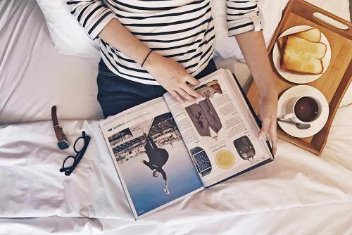 a woman sitting on a bed reading a magazine at My Studio Hotel Losari Makassar in Makassar
