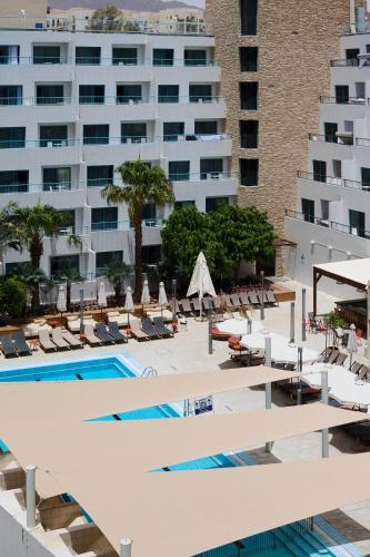 a swimming pool with lounge chairs and a large building at Neve Eilat Hotel By Atlas Hotels in Eilat
