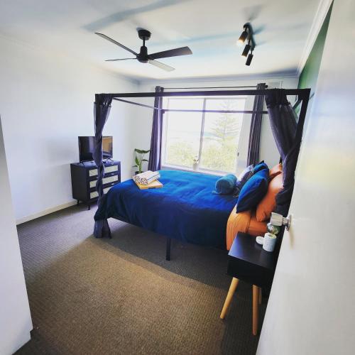 a bedroom with a bed with a blue comforter and a window at Casa Luna Beachside Apartment in Henley Beach South