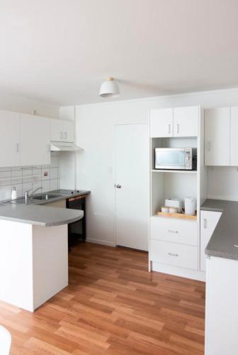 a white kitchen with white cabinets and a wooden floor at Cute one bedroom near Waterview in Auckland