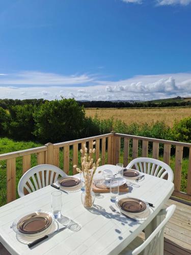 une table blanche avec des assiettes et des verres sur une terrasse dans l'établissement Camping le Kergorz, à Plomodiern
