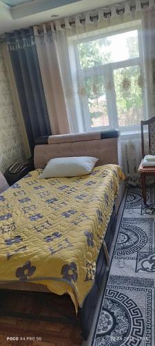 a bedroom with a bed with a yellow blanket and a window at Guest House Oimo in Balykchy
