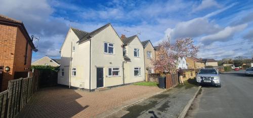 a white house with a car parked on a street at 6 Bedroom Spacious villa, Free Parking in Byfleet