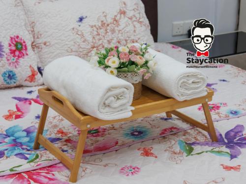 クチンにあるStaycation Homestay 51 Luxe Garden Homestayの花が飾られたテーブルの上にタオルが2枚置かれたベッド