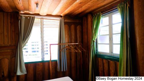 a room with wooden walls and a window with green curtains at Baey Bōgan Homestay in Sagada