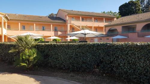 une haie devant un bâtiment avec des parapluies dans l'établissement Résidence les jardins de la mer 20230 marine de bravonne, à Linguizzetta
