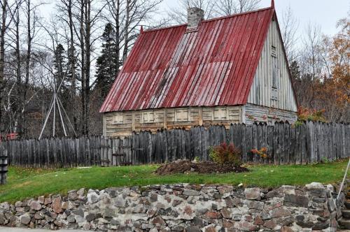 an old barn with a red roof and a fence at Hotel Le Pionnier in Tadoussac