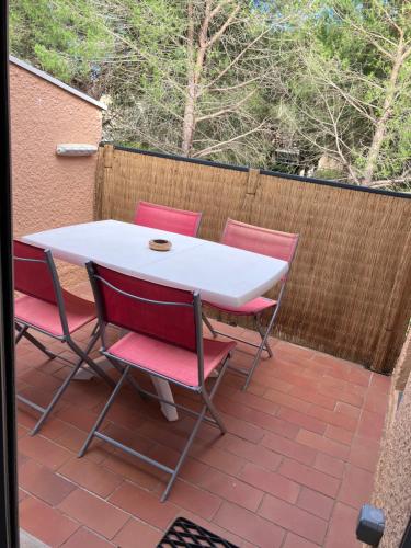 une table blanche et quatre chaises rouges sur la terrasse dans l'établissement Appartement vue Piscine sous les Pins, au Cap d'Agde