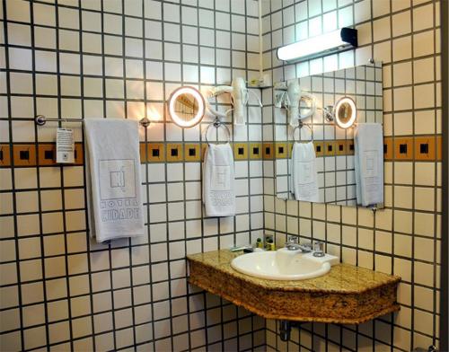 a bathroom with a sink and towels on a tiled wall at Hotel Cidade in Passos