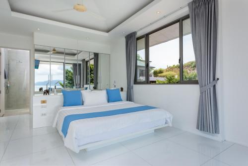 a white bedroom with a large bed with blue pillows at Villa Oceane in Thong Son Beach