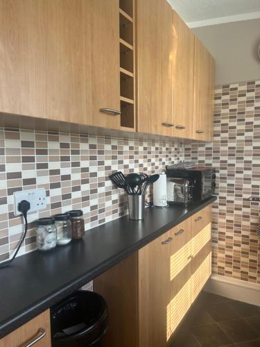 a kitchen with wooden cabinets and a black counter top at Driftwood & Daisies- Red Buoy Retreat in Hemsby