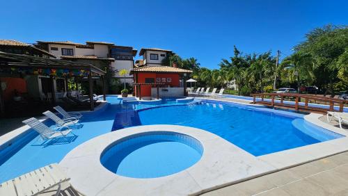 a large swimming pool with chairs and a building at Apartamento Cachalote - Terraces Porto das Baleias - Praia do Forte in Praia do Forte