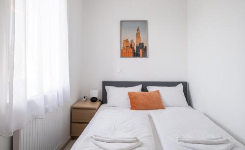 a bedroom with a bed with white sheets and an orange pillow at Aranymandula apartmanok in Balatonakali