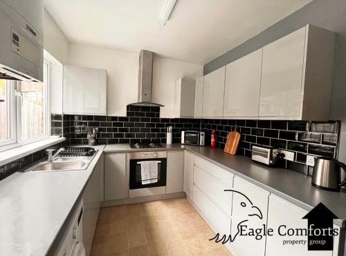 a kitchen with white cabinets and black tiles on the wall at 5 Bedroom House-20 percent off monthly stays in Neepsend