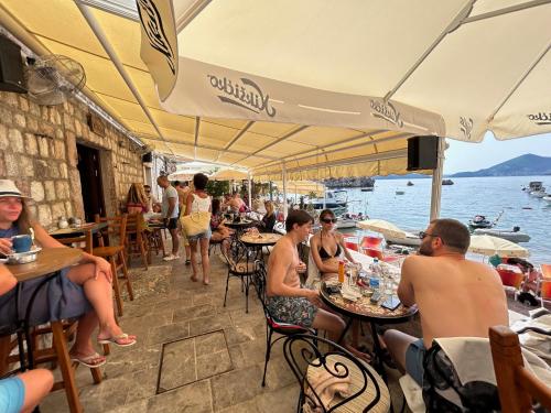 a group of people sitting at tables near the water at Private Patio Przno Steps to Beach 2 Bedroom 2 Parkings BBQ Villa Olive in Sveti Stefan