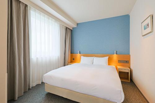 a bedroom with a white bed and a blue wall at JR Kyushu Hotel Miyazaki in Miyazaki