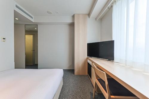 a bedroom with a bed and a desk with a television at JR Kyushu Hotel Miyazaki in Miyazaki