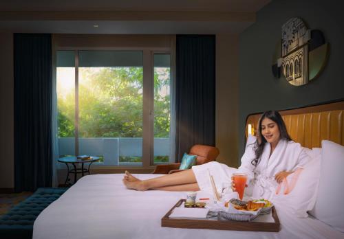 a woman sitting on a bed with a tray of food at Welcomhotel by ITC Hotels, Cathedral Road, Chennai in Chennai