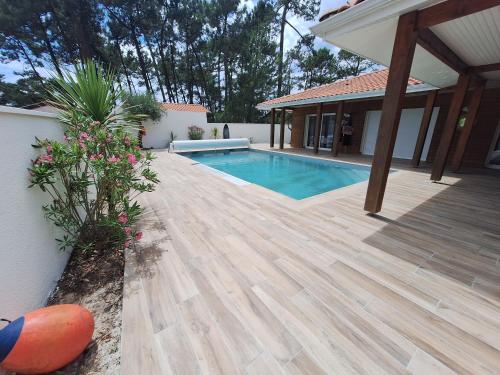 une arrière-cour avec une terrasse en bois et une piscine dans l'établissement Villa_palms_mimizan_plage jolie villa 12 personnes, piscine chauffée et plage à pied, à Mimizan
