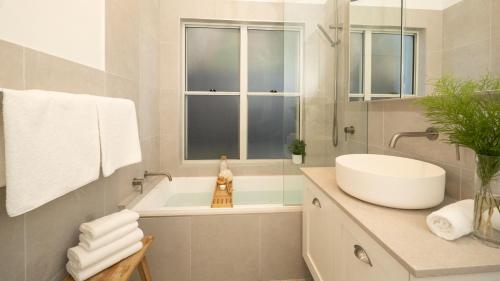 ein weißes Badezimmer mit einem Waschbecken, einer Badewanne und einem Spiegel in der Unterkunft Sunshine Cottage in Culburra Beach