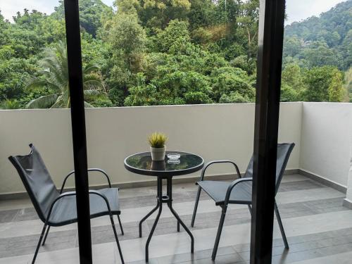 a table and chairs on a balcony with a view of trees at Cosy Designer's Home By The Mountain in Lumut