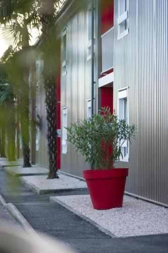 a plant in a red pot next to a building at Brit Hotel Essentiel Pau Lescar in Lescar