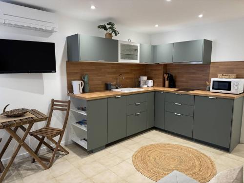 une cuisine avec des placards gris, un four micro-ondes et une table dans l'établissement L'appartement Le Levant au Lavandou, au Lavandou