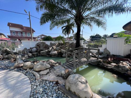 Un puente sobre un estanque con rocas y una palmera. en DeGarden House Bangi, en Kajang