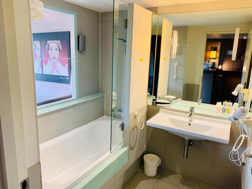 a bathroom with a sink and a bath tub and a mirror at Standing Hotel Suites by Actisource in Roissy-en-France