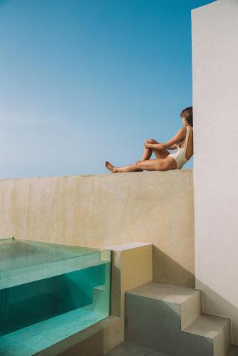 a woman sitting on a wall next to a swimming pool at Domes White Coast Milos, Adults Only - Small Luxury Hotels of the World in Mytakas