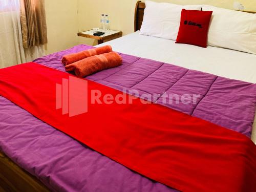 a bed with a red and purple blanket on it at Sahil inn Syariah Prawirotaman RedPartner in Timuran