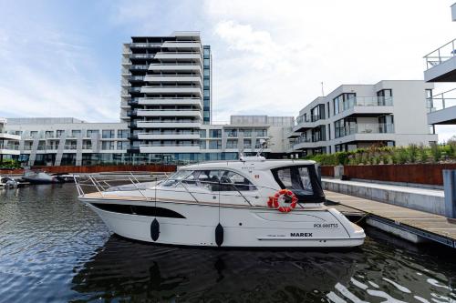 a white boat is docked in the water with buildings at Sol Marina Resort Wyspa Sobieszewska II - LoftAffair Collection in Wiślinka