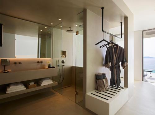 a bathroom with a shower and a robe on a rack at Domes White Coast Milos, Adults Only - Small Luxury Hotels of the World in Mytakas